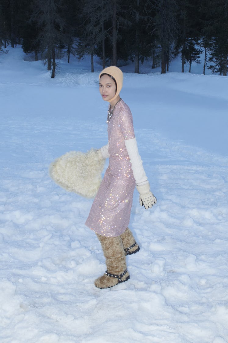 A model in a violet shimmery dress, fur boots, white gloves and a matching bag by Miu Miu 