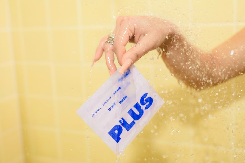 a hand in a shower holds out a white package of plus