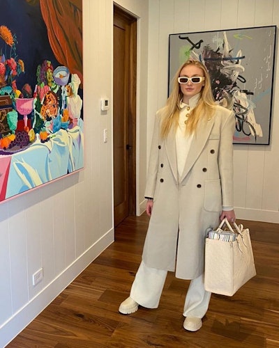 Sophie Turner wearing a trench coat and white trousers.