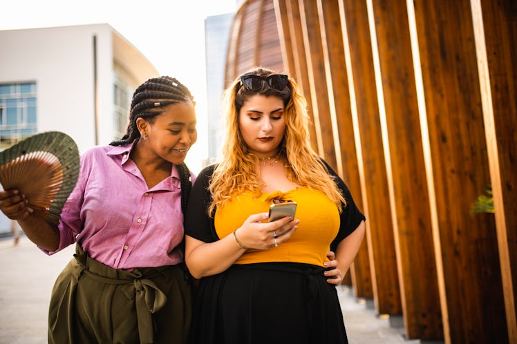 Two women look at a phone outside. Use these funny WhatsApp group names for your friend group chats.