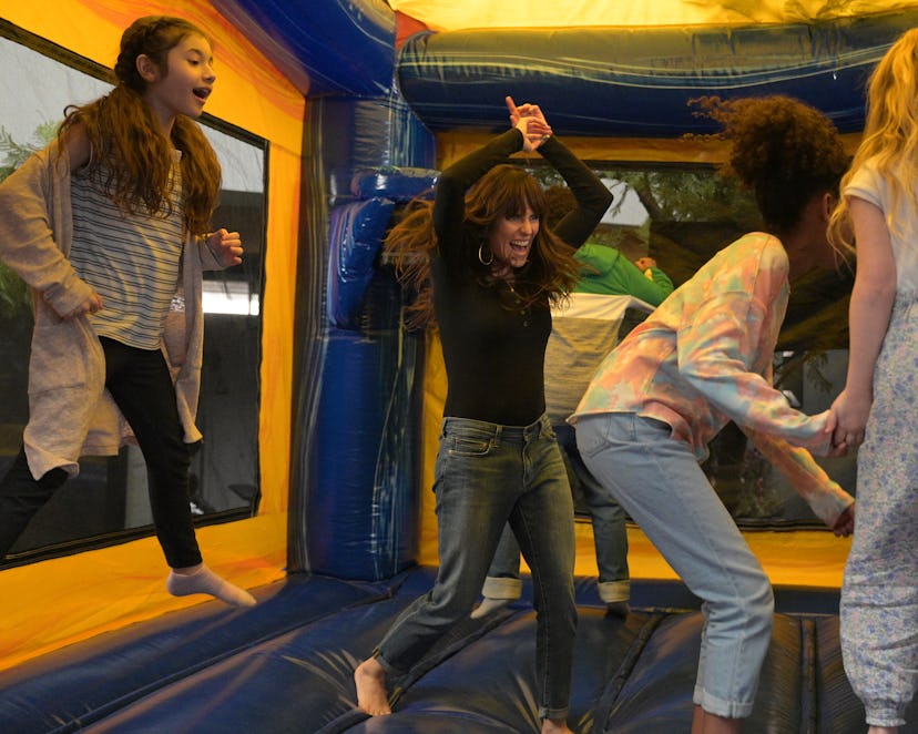 Karla Souza is jumping in a bounce house with several kids in an episode of HOME ECONOMICS called “B...