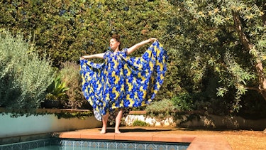 Kathryn Hahn in a big, flowing blue and yellow dress, that she holds up in the air like wings 