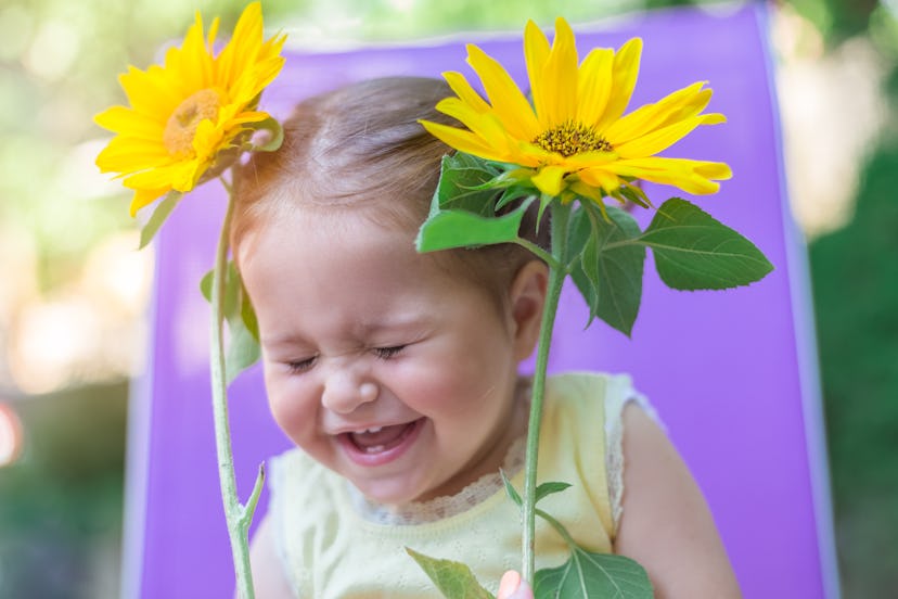 May baby names, like Birdie, would fit this toddler girl laughing while holding yellow flowers.