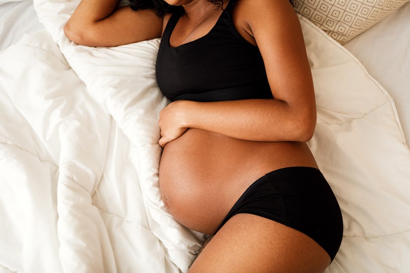 pregnant woman in black bra and panties, lying on her side on a bed