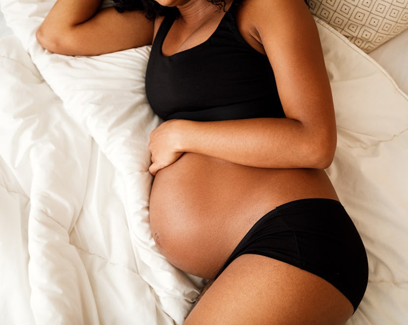 pregnant woman in black bra and panties, lying on her side on a bed