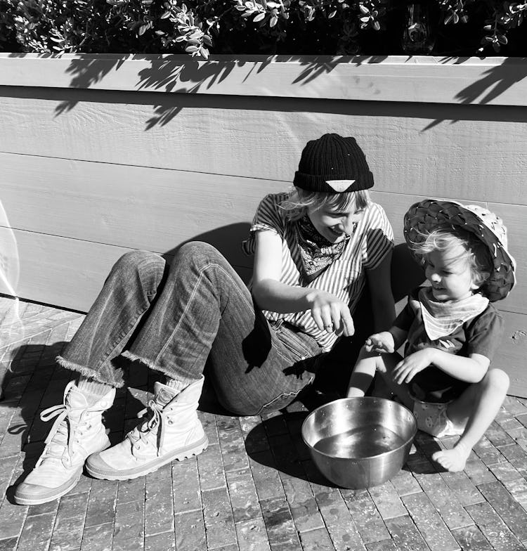 a black-and-white photo of Mickey Sumner with her son, Akira, sitting outside, playing with a bowl o...