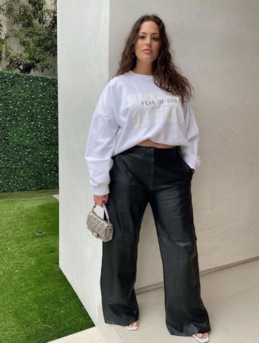 Model Ashley Graham wearing jeans, long-sleeve white top, and a pair of sandals.