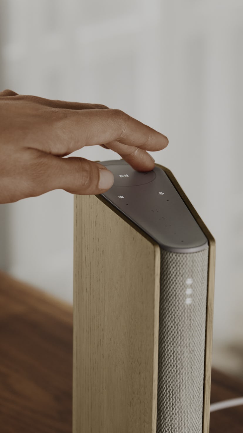 A hand is touching a compact Bang and Olufsen Emerge speaker.
