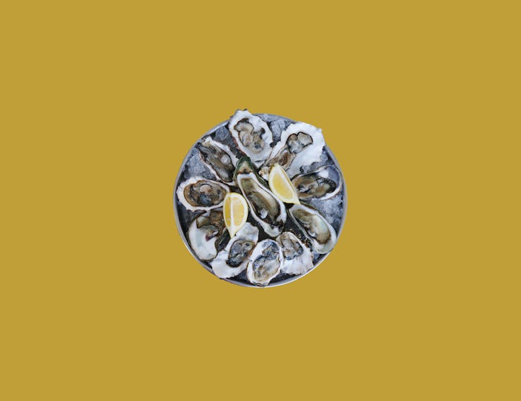 Raw oyster plate with two lemons on a yellow background