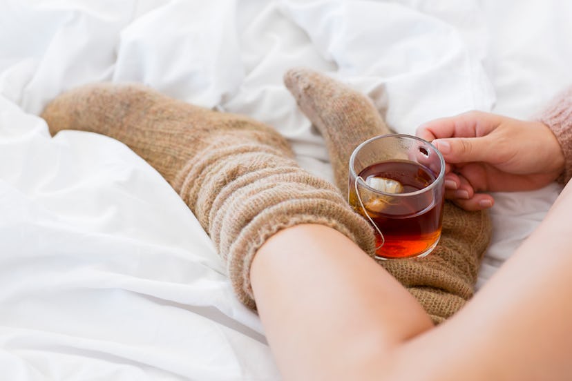 Close-up of a woman with cup of herbal tea in bed dealing with period cramps at night