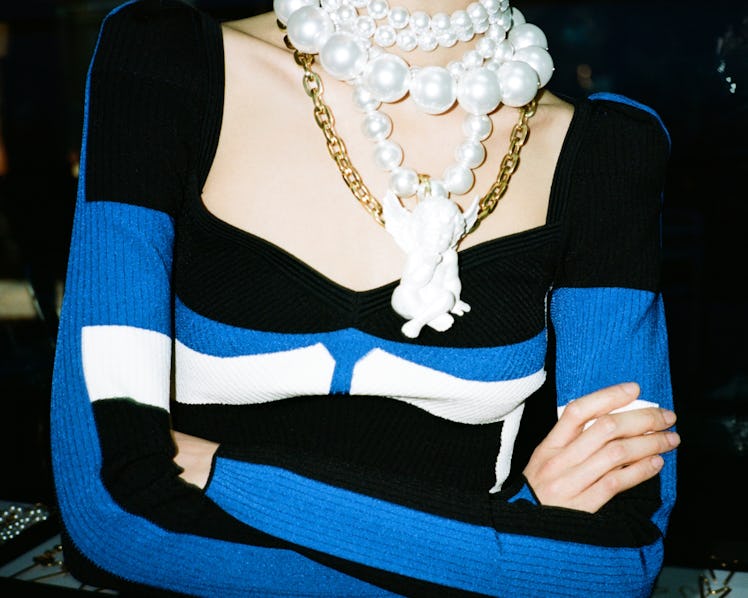 A close-up of a model wearing a black-white-blue dress with large layered pearl necklaces by Alber E...