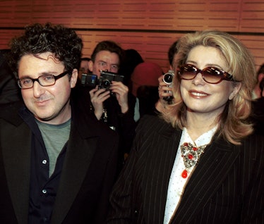 Alber Elbaz and Catherine Deneuve posing together with a group of people taking photos behind them