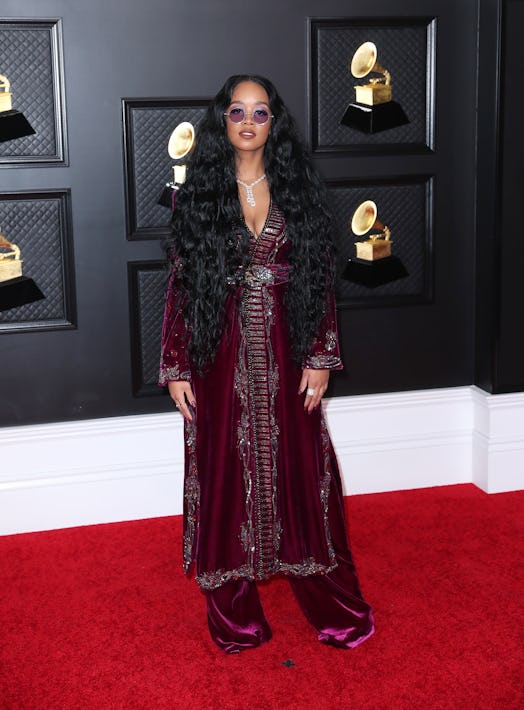 H.E.R. at the 2020 Grammy Awards in a maroon, long-sleeved velvet dress with matching pants and circ...