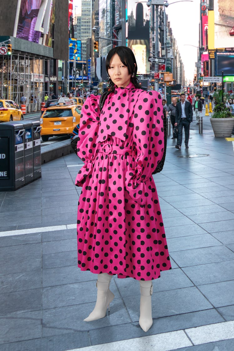  A model wearing Balenciaga's pink polka dots dress while standing in the street.