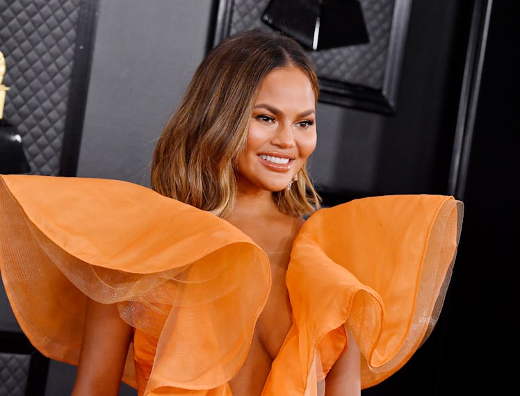 Chrissy Teigen smiling in an orange tulle gown at the Grammy Awards