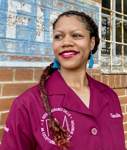 Chavalia Dunlap-Mwamba smiling with braided hair, blue earrings and a burgundy shirt