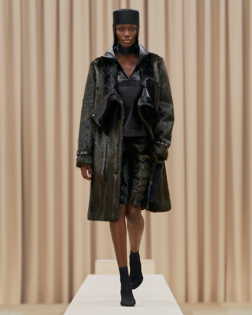 A model wearing a black leather hoodie, a fur coat, and a hat at the London Fashion Week