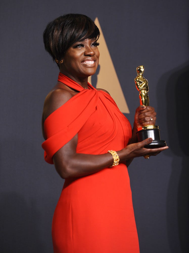 Viola Davis holding her Oscar in a red dress and a short haircut with bangs swept to the side 