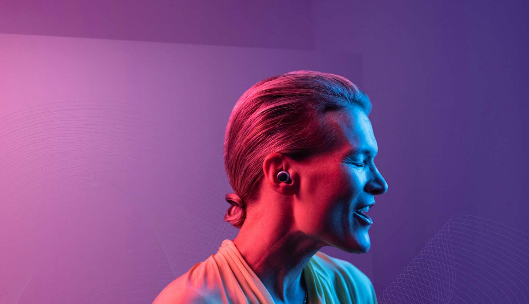 A woman is seen under pink, purple, and blue lights with a hearing aid in her ear.