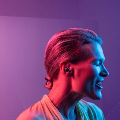 A woman is seen under pink, purple, and blue lights with a hearing aid in her ear.