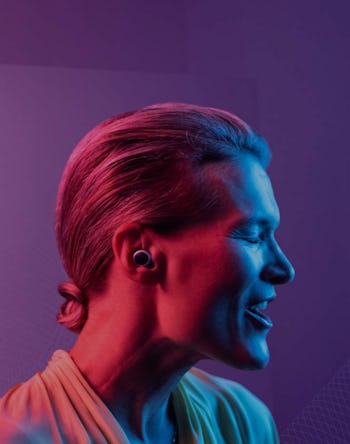 A woman is seen under pink, purple, and blue lights with a hearing aid in her ear.