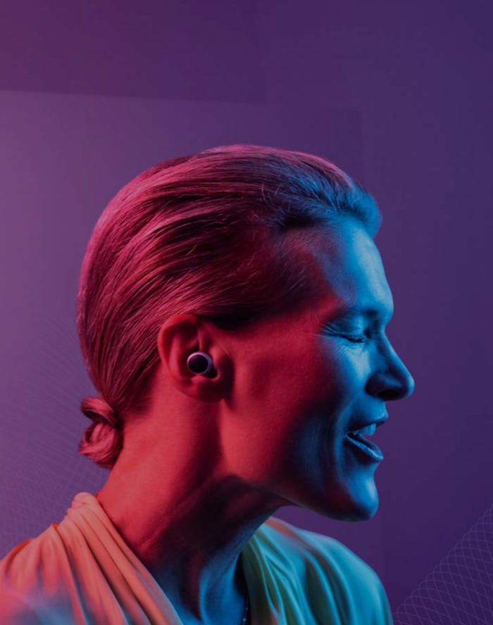 A woman is seen under pink, purple, and blue lights with a hearing aid in her ear.