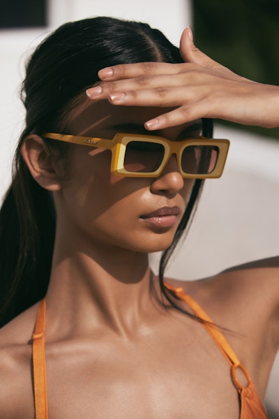 Model wearing big orange sunglasses posing for a picture with her hand on the forehead.