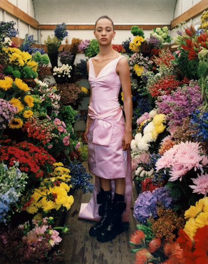 Model posing in silk pink dress surrounded by piles of flowers