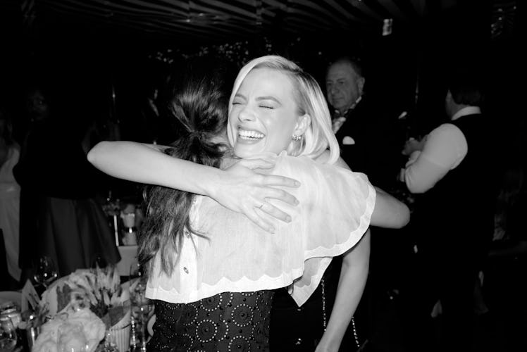 Margot Robbie smiling and hugging a woman at Chanel’s Pre-Oscars Dinner