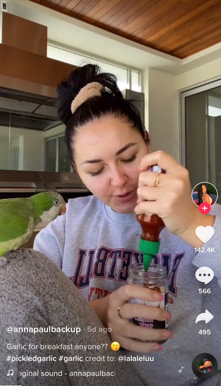 A woman puts Sriracha sauce in a jar of pickled garlic for TikTok. 