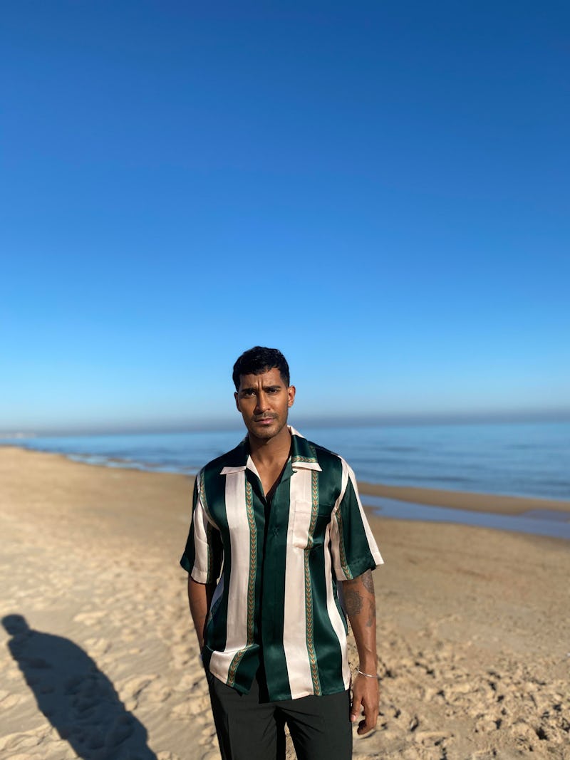 Lee Juggernauth, presenter of Channel 4's A place in the sun pictured on a beach in a stripey shirt