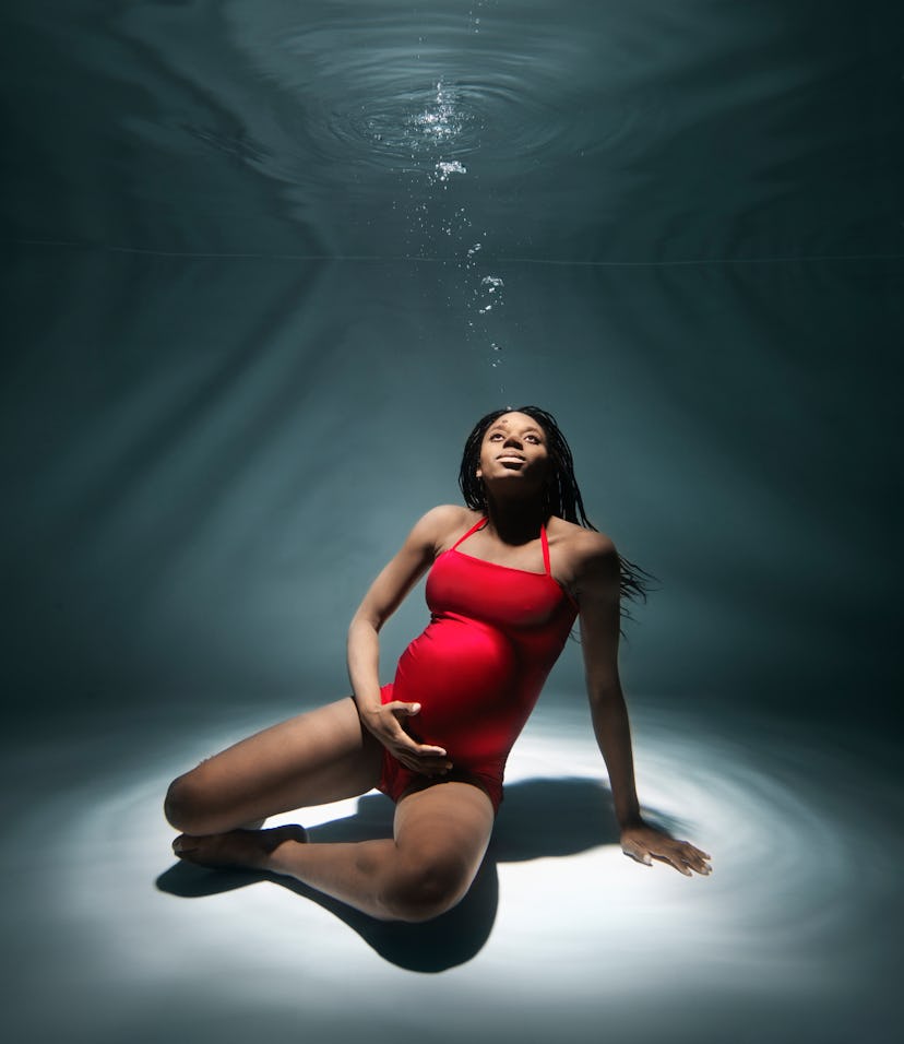 pregnant woman in red bathing suit, sitting at the bottom of a swimming pool