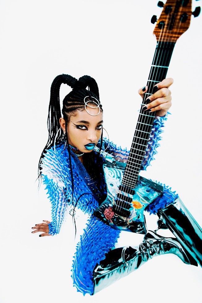 A portrait of WILLOW (aka Willow Smith) in an electric blue outfit sitting while holding a blue elec...