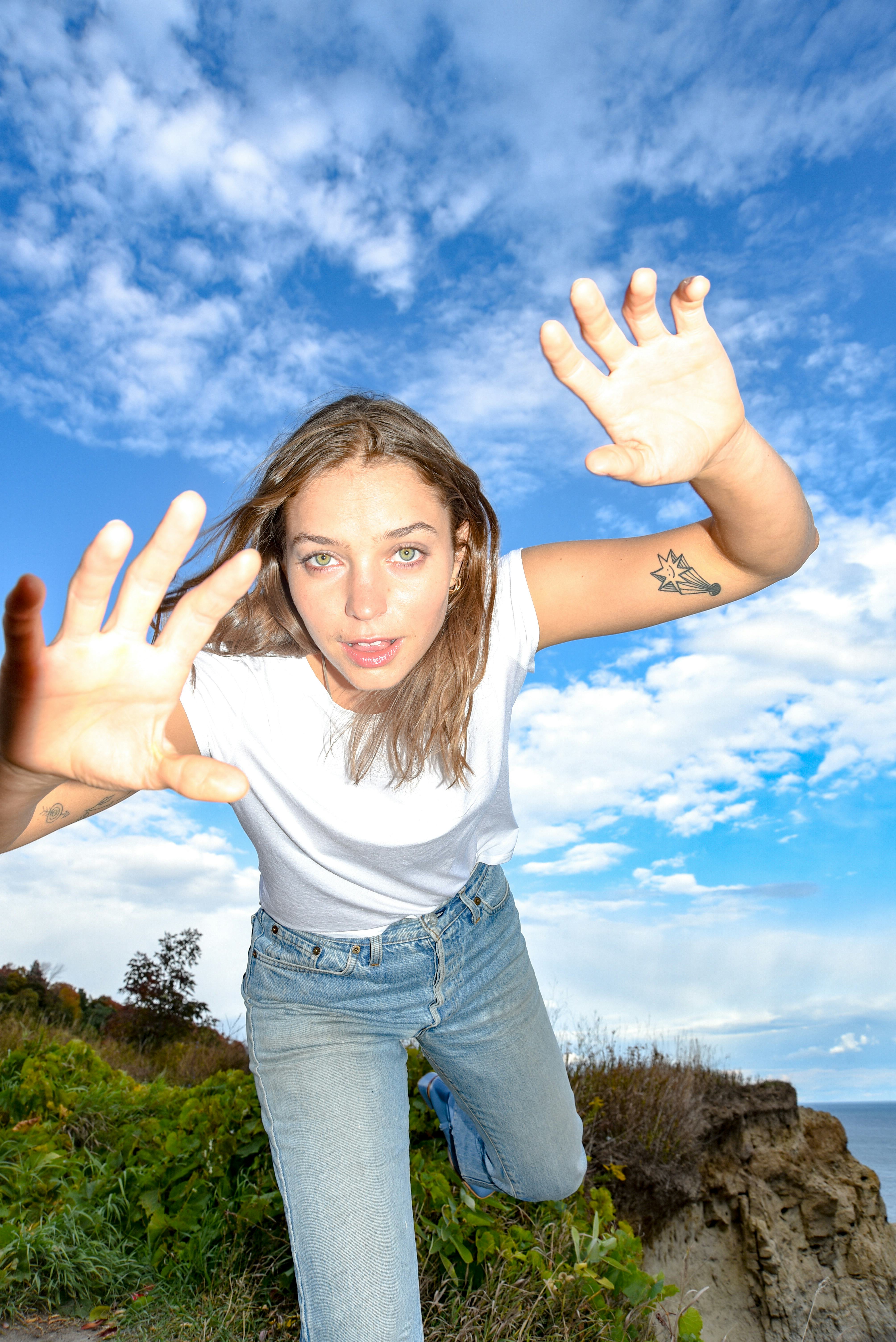 A picture of Madeline Link. She's wearing a white tee tucked into jeans and is lunging at the camera...
