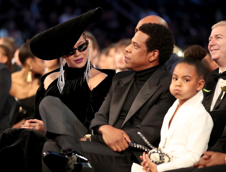 Beyonce in a black dress and hat, Jay-Z in a black suit, and Blue Ivy Carter in a white dress sittin...