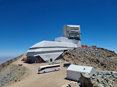 Photo shows the large summit facility building housing the telescope being built atop a mountain nea...