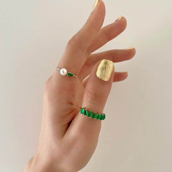 Gold nail polish with pearl and jade rings modeled on hand 