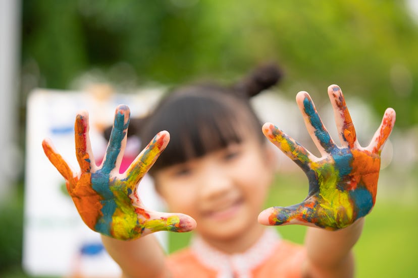 Little girl holding up her paint-covered hands, a finger-painted project is a great DIY mother's day...