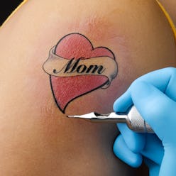 A close-up of an in-progress tattoo on a person's arm that reads, "Mom"