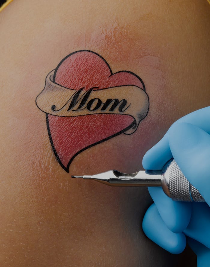A close-up of an in-progress tattoo on a person's arm that reads, "Mom"