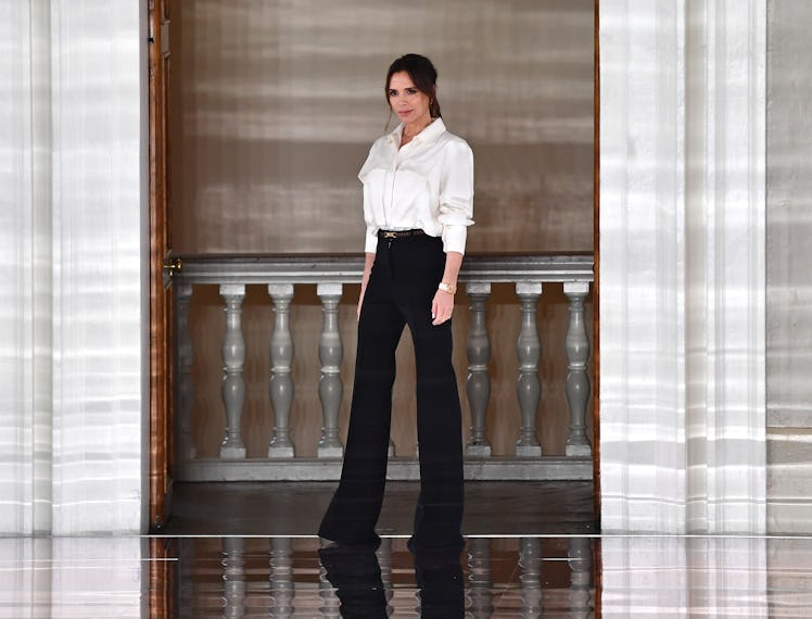Victoria Beckham standing while wearing a white shirt and black pants