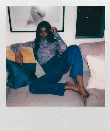 ctress Ego Nwodim wearing blue pants and a colorful shirt while sitting on a gray couch