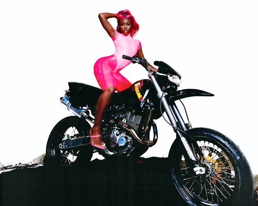 A portrait of Bree Runway in a skintight pink catsuit posing on a motorcycle. 