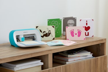 The Cricut Joy sits on a desk next to DIY cards made from it. 
