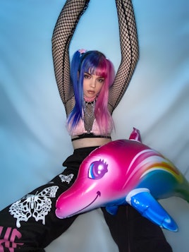 A photo of Rakky Ripper. Her pigtails are dyed half-blue and half pink, and an inflatable pink dolph...