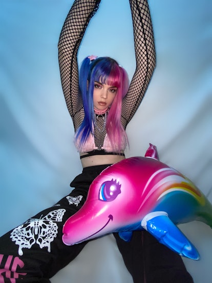 A photo of Rakky Ripper. Her pigtails are dyed half-blue and half pink, and an inflatable pink dolph...