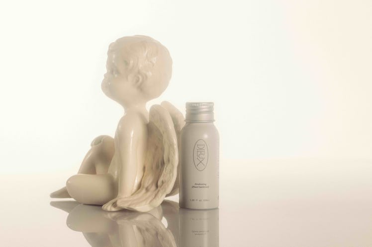 A baby boy with wings sculpture next to a Dieux hand sanitizer bottle