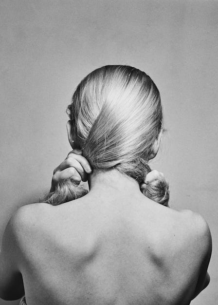 Model posing with her head turned to wall, showing her naked back and hair. 