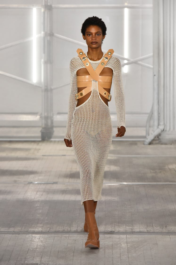 A model walking the Dion Lee runway at New York Fashion Week in a white sheer dress with beige belts...