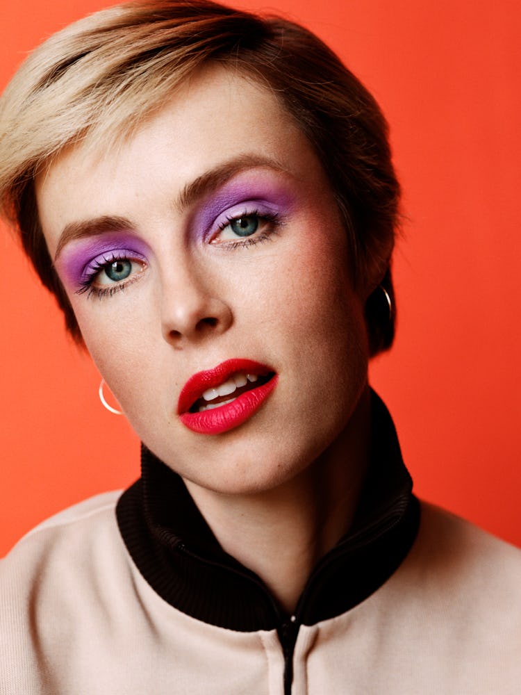 Edie Campbell in a beige and black bomber jacket and purple eyeshadow with red lipstick 